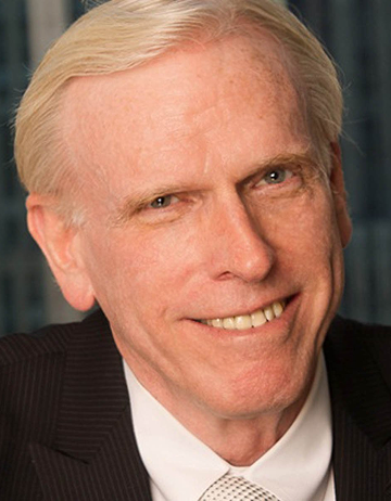 Oliver is pictured against a dark, textured background. He is smiling and weating a black jacket over a white collared shirt with a black and white dotted tie