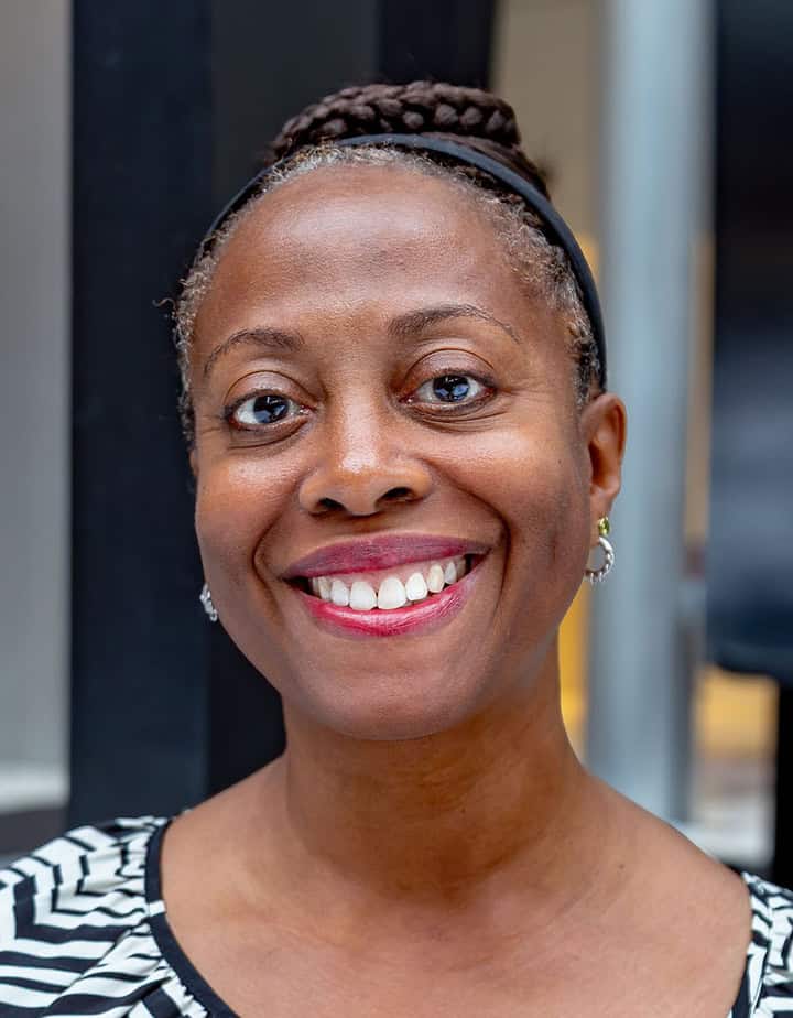 Aerica is pictured in an open space with a textured background. She is smiling and wearing a black and white blouse and silver earrings.